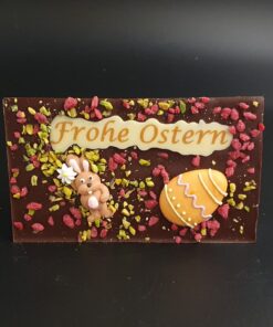 Zartbitter-Ostertafel mit bunter Zuckerdekor, kristallisierten Rosenblüten und gehackten Pistazien und Schriftzug Frohe Ostern