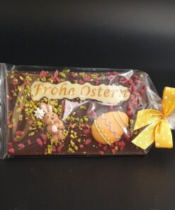 Zartbitter-Ostertafel mit bunter Zuckerdekor, kristallisierten Rosenblüten und gehackten Pistazien und Schriftzug Frohe Ostern, verpackt mit Schleife