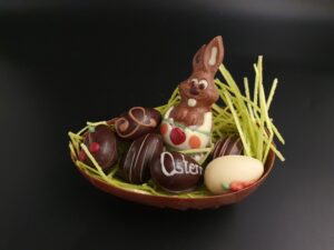 Halbes Osterei aus Vollmilch-Schokolade, gefüllt mit 6 Pralinen-Ostereiern und einem kleinen Osterhasen aus Vollmilch-Schokolade